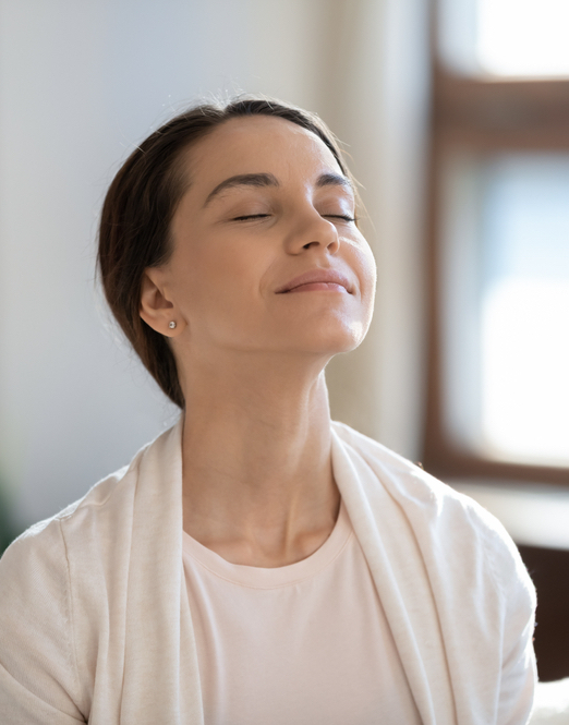 Calm leisure. Content young woman spending time at home alone, sitting on sofa with eyes closed in delight, breathing fresh cool air because of working conditioner, giving face to sunlight from window